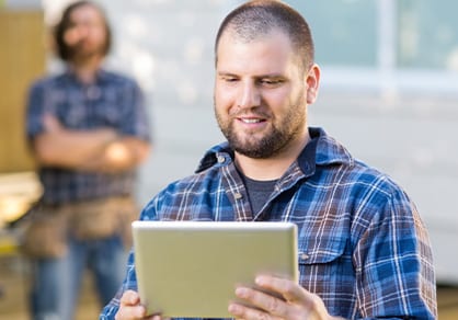 Mid adult carpenter using digital tablet with coworker standing in background at construction site